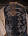 Close-up of a black leather boot shaft with intricate western stitching on a wooden surface.