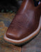 Brown leather boot with western stitching on a stone surface