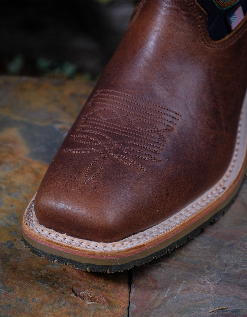 Brown leather boot with western stitching on a stone surface