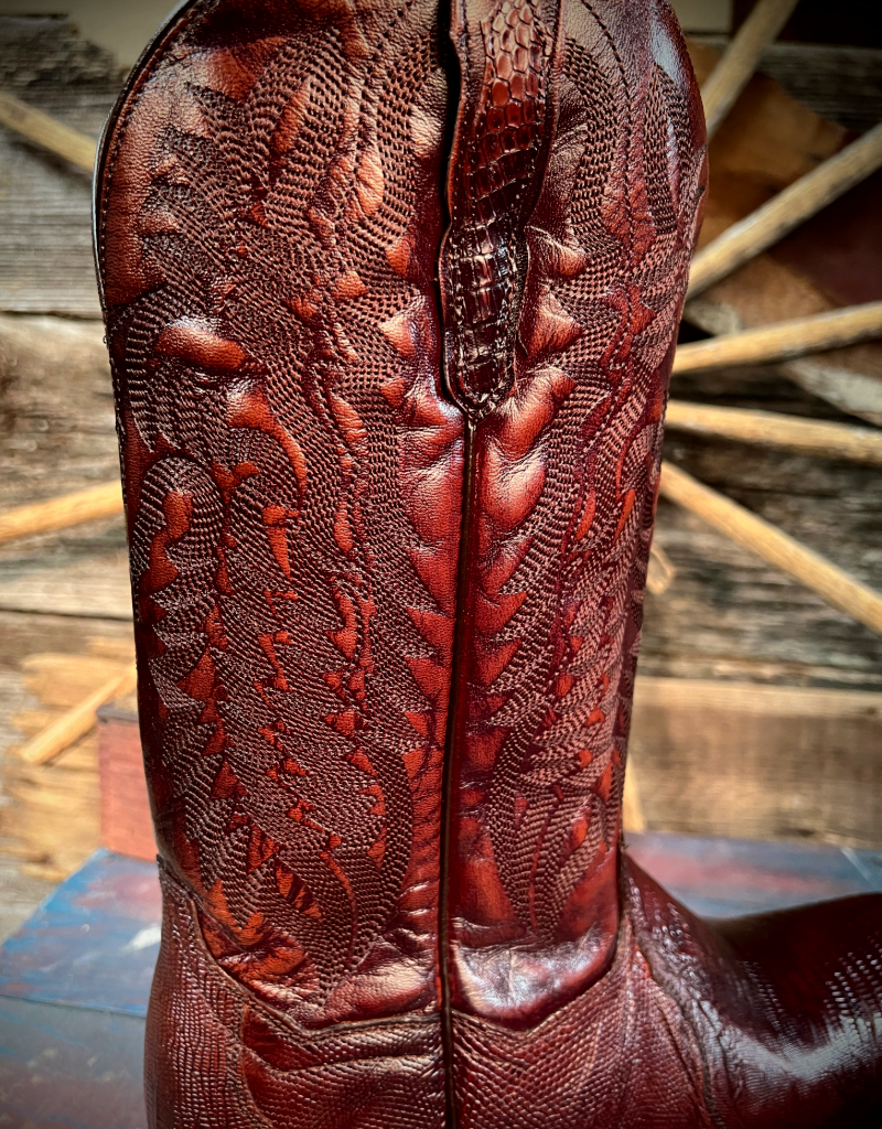 Close-up of a brown/burgundy leather boot with intricate western stitching on a wooden surface.