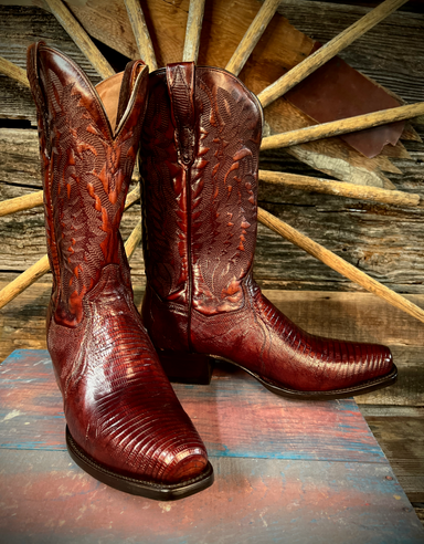 Pair of brown cowboy boots on a wooden surface with a wagon wheel in the background