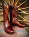 Pair of brown cowboy boots on a wooden surface with a wagon wheel in the background
