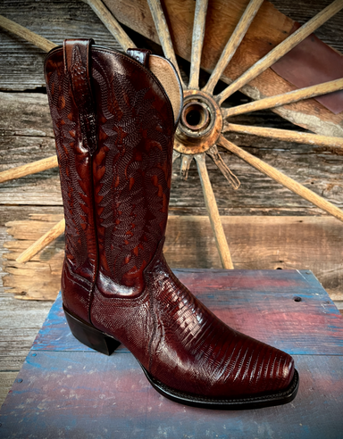 Brown/burgundy cowboy boot on a wooden surface with a rustic background