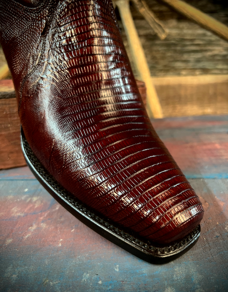 Close-up of a rich brown boot with lizard leather on a wooden surface.