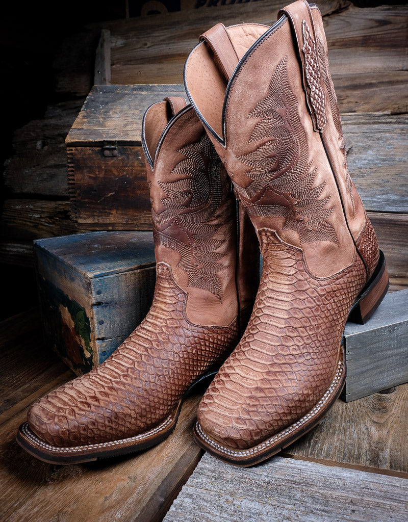 Two tan colored square toe western boots resting on wood planks