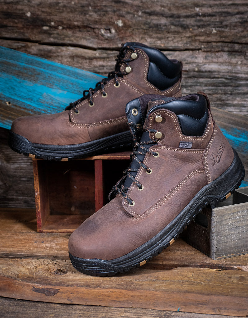 Brown leather boots with black soles on a wooden surface