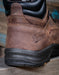 Brown leather boot with black sole featuring Danner logo on a wooden surface.
