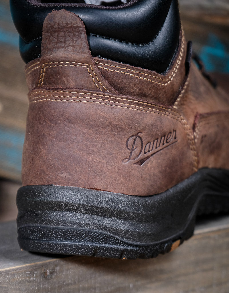 Brown leather boot with black sole featuring Danner logo on a wooden surface.