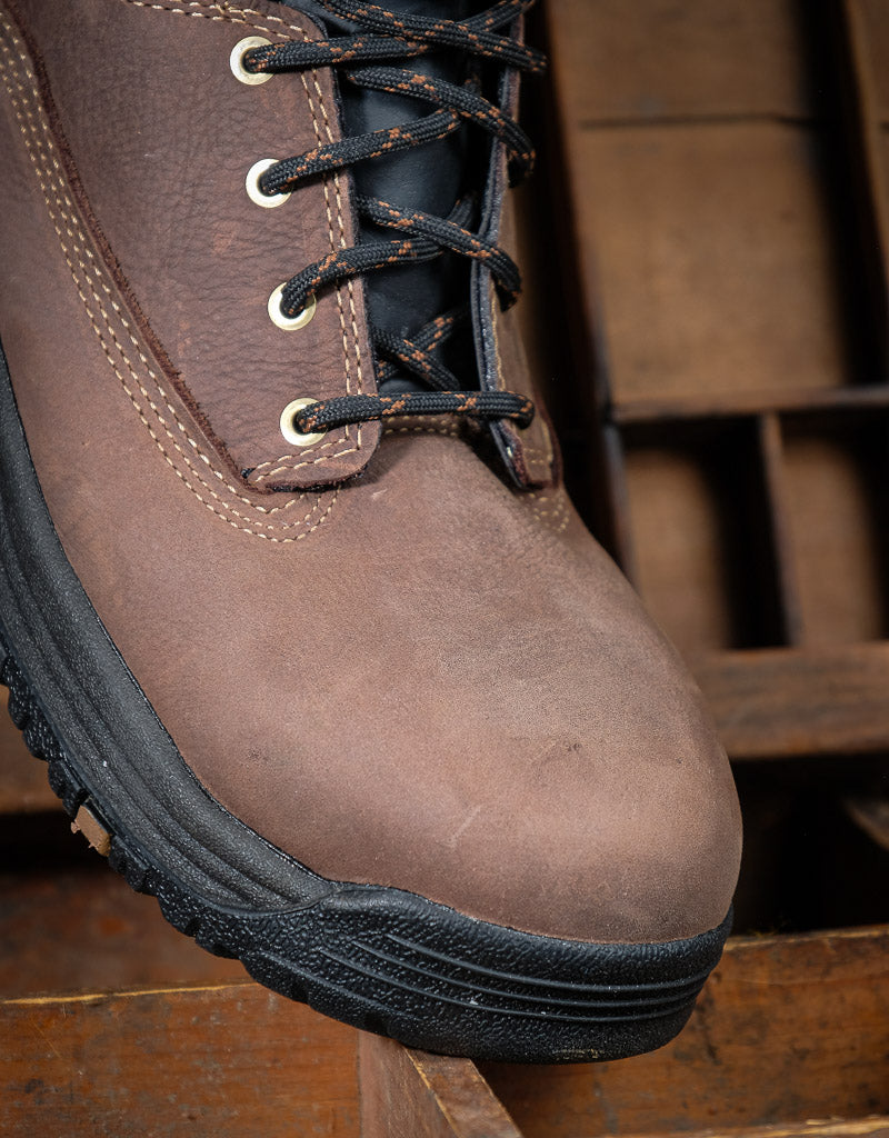 Brown leather boot with black sole on a wooden surface