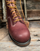 Brown leather boot with yellow laces on a wooden surface