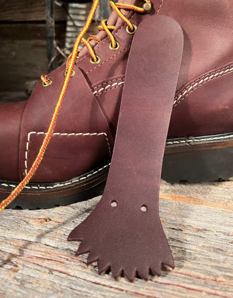 Brown leather removable tongue on a wooden surface next to a brown leather boot with yellow laces.