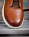 Brown leather shoe with white sole on a wooden surface