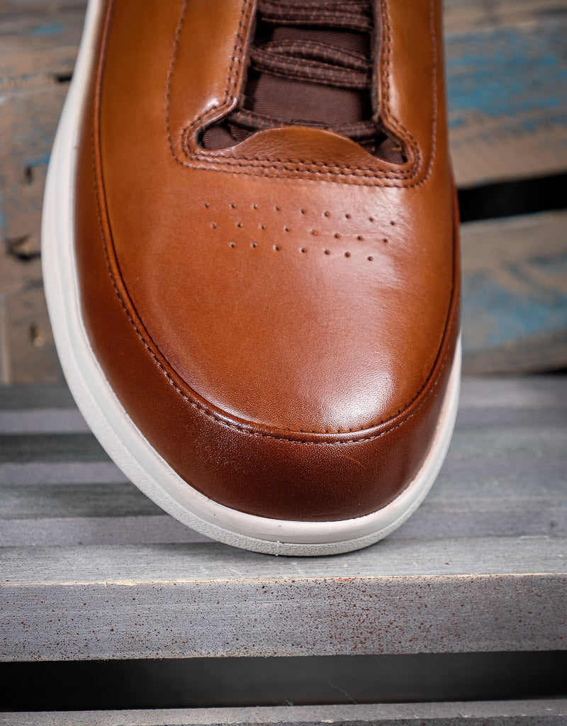 Brown leather shoe with white sole on a wooden surface