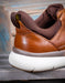 Brown leather shoe with white sole on a wooden surface