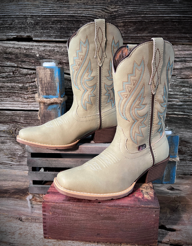 Pair of bone colored cowboy boots with intricate designs on a wooden stand against a rustic wooden background.