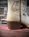 Close-up of an off white cowboy boot with turquoise stitching on a wooden surface.