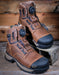 Pair of brown work boots with black soles on a wooden background