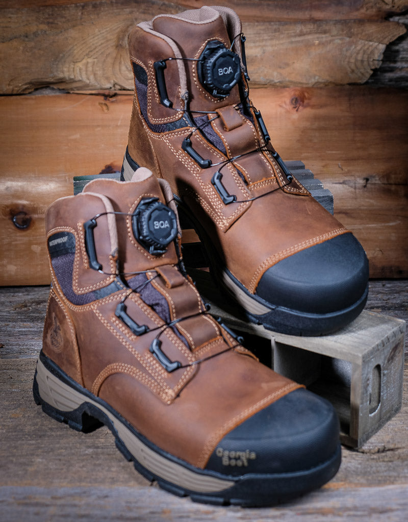 Pair of brown work boots with black soles on a wooden background