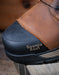 Close-up of a brown leather boot with a black sole on a wooden surface.