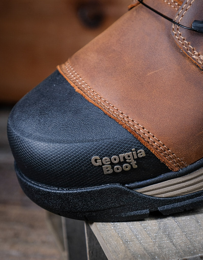 Close-up of a brown leather boot with a black sole on a wooden surface.