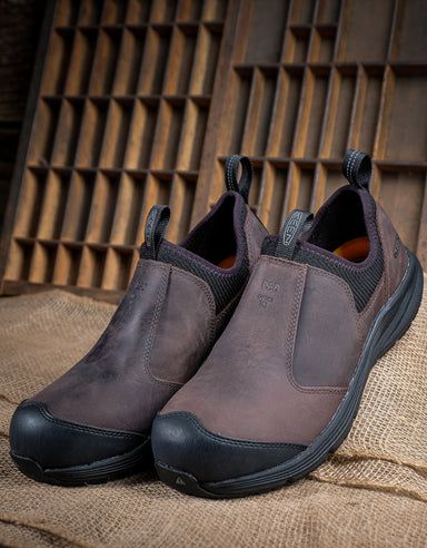 Pair of brown slip-on shoes with black soles on a rustic wooden background