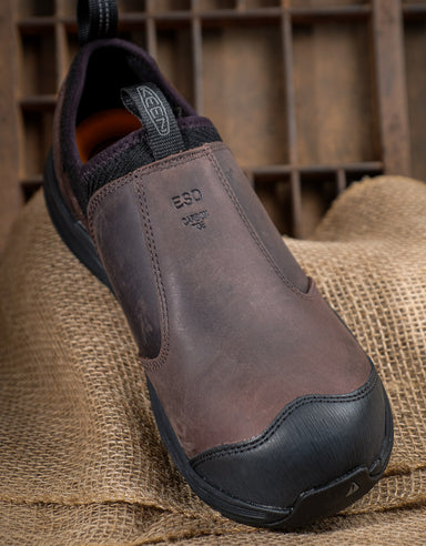 Brown slip-on shoe with black sole on a rustic wooden background