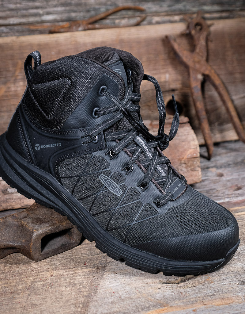 Black hiking boot on a wooden surface with rusty tools in the background