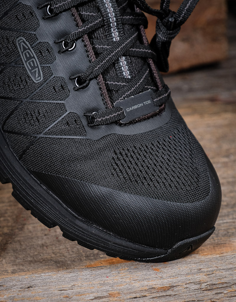 Black hiking style  boot toe with KEEN brand logo on a wooden surface