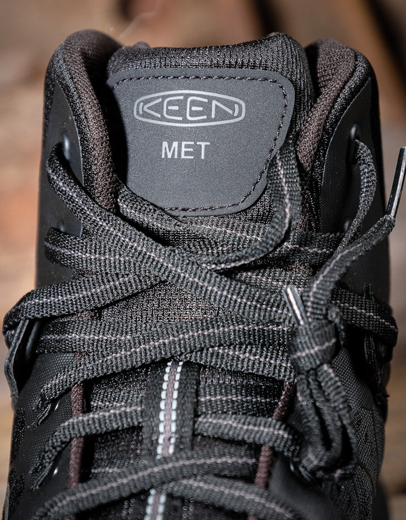 Close-up of a black KEEN work boot with laces and 'KEEN' branding plus a logo that says 'MET'