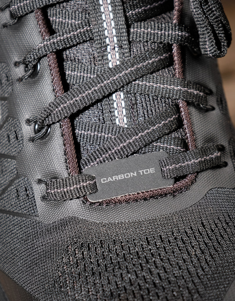 Close-up of a black laced shoe with a 'Carbon Toe' label on a blurred background
