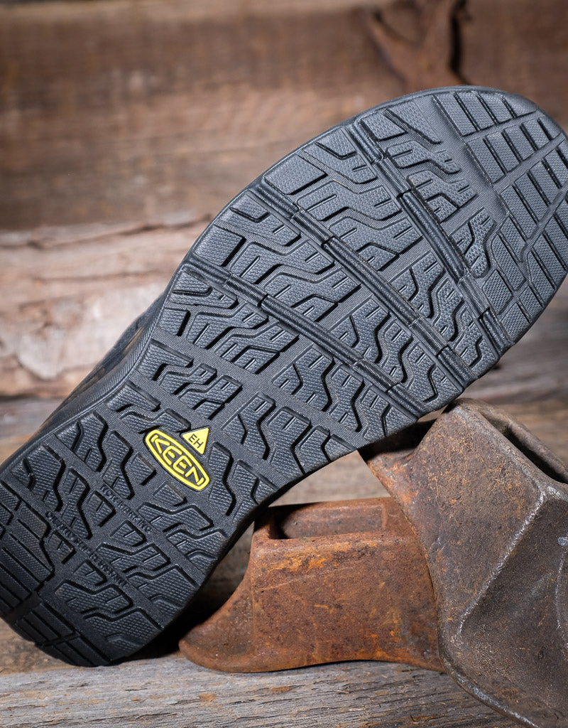 Close-up of a black work boot sole with a brand logo on a rustic wooden background