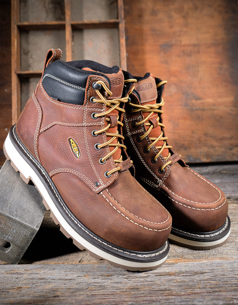 Pair of brown leather work boots with laces on a wooden background