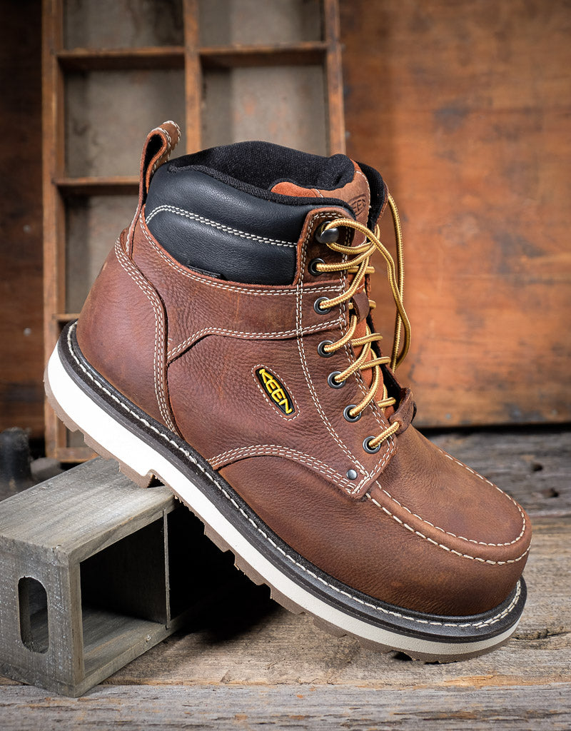 Brown work boot with a visible Keen brand logo on a wooden background