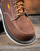 Brown leather boot with yellow laces on a wooden surface