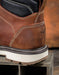 Close-up of a brown leather boot with white sole on a wooden surface