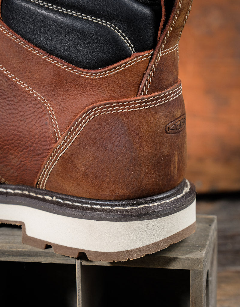 Close-up of a brown leather boot with white sole on a wooden surface