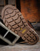 Close-up of a brown leather boot sole with a visible Keen brand logo on a wooden surface.