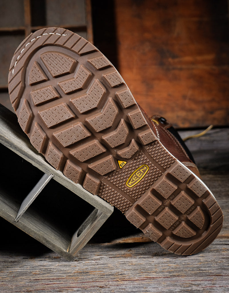 Close-up of a brown leather boot sole with a visible Keen brand logo on a wooden surface.