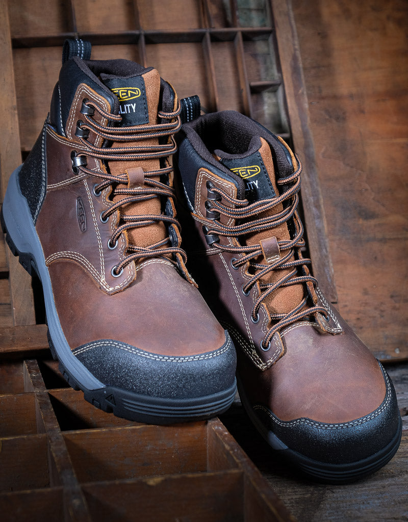 Pair of brown leather work boots with black and grey soles on a wooden background