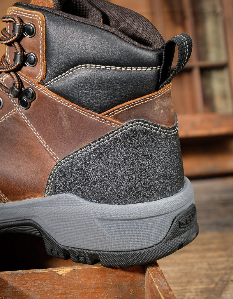 Brown and black hiking boot with gray sole on a wooden surface