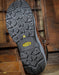 Close-up of a brown leather boot with a textured black sole on a wooden background