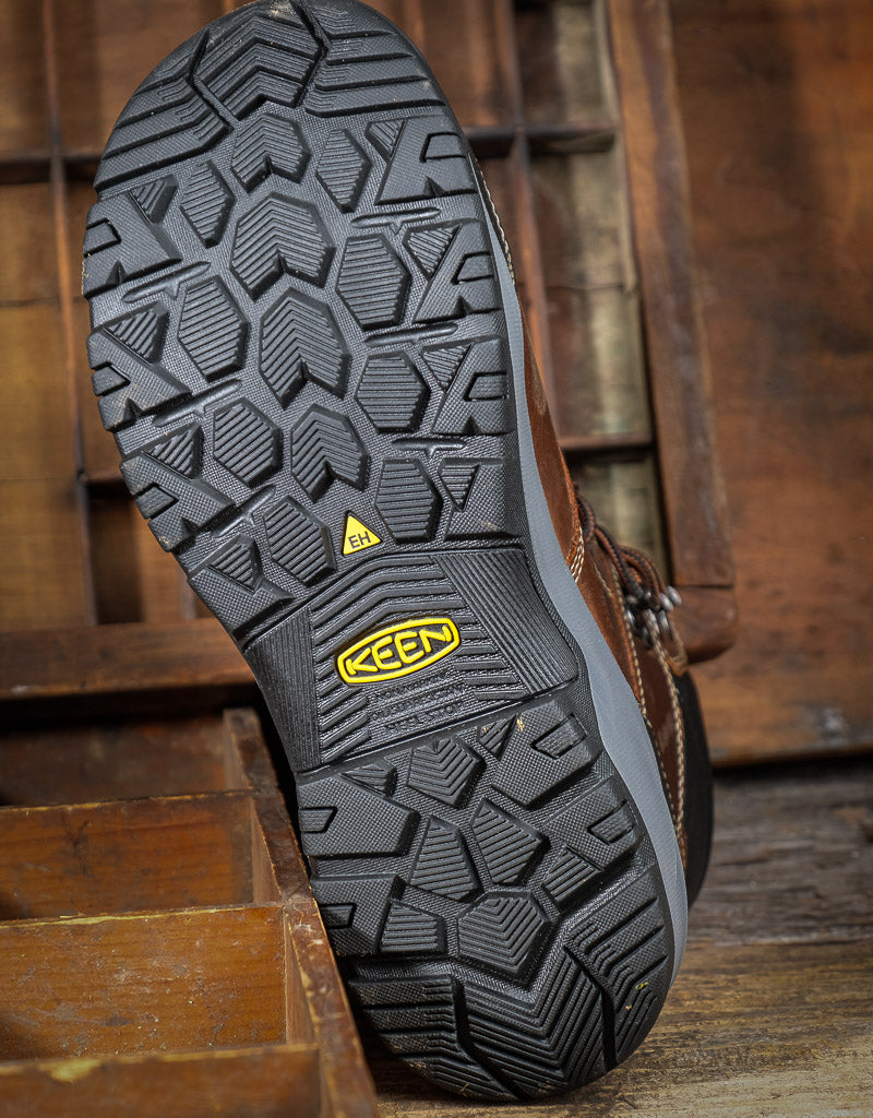 Close-up of a brown leather boot with a textured black sole on a wooden background