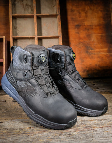 Pair of black and blue Keen boots on a wooden surface with a rustic background