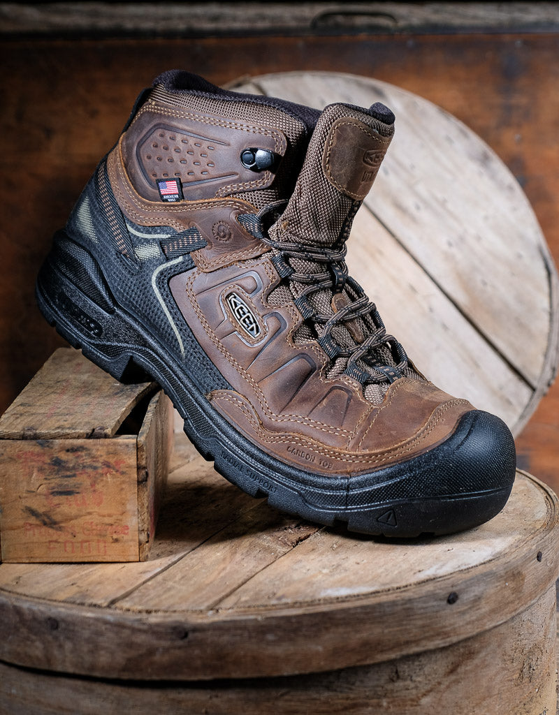 Brown hiking boot with black sole on a wooden surface