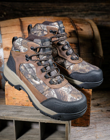 Camouflage work boots on a wooden surface with a rustic background