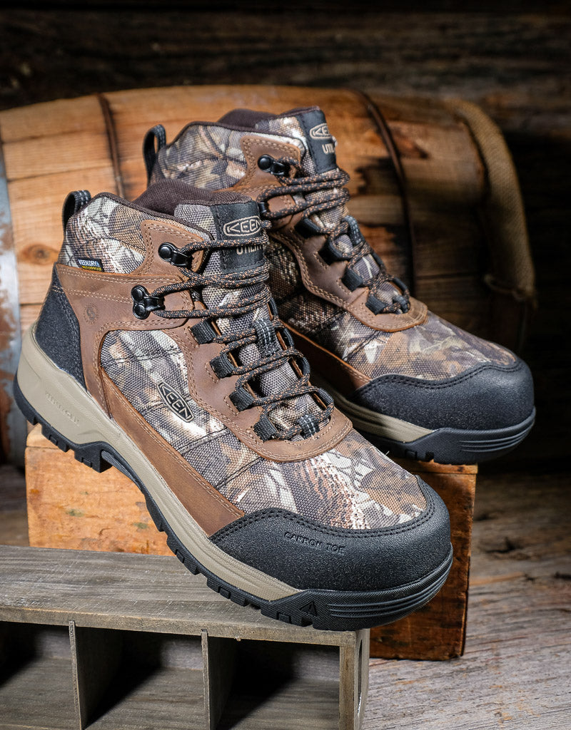 Camouflage work boots on a wooden surface with a rustic background