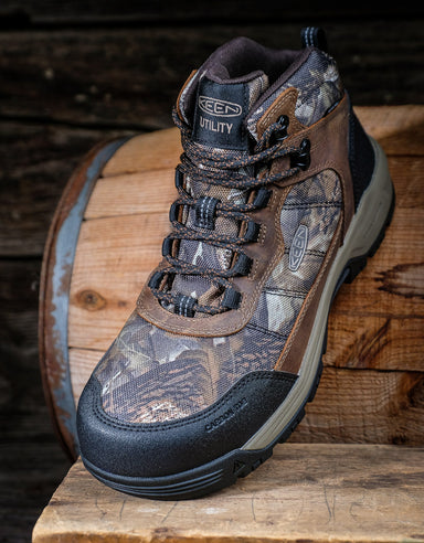 Camouflage hiking boot on a wooden surface with a rustic background