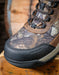 Camouflage hiking boot with black sole on a wooden surface