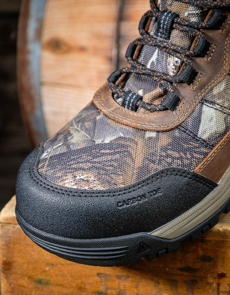Camouflage hiking boot with black sole on a wooden surface