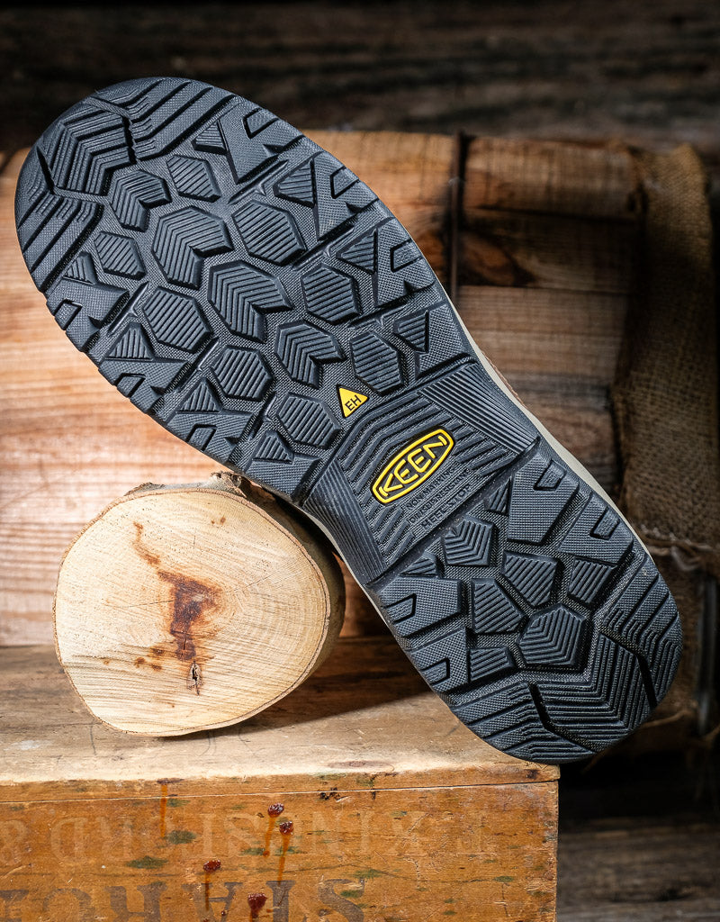 Close-up of a black rubber sole with a Keen brand logo on a wooden surface
